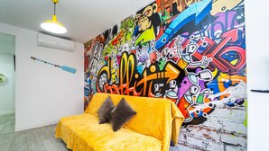 Une pièce avec un canapé jaune, un mur décoré de graffitis colorés et un luminaire suspendu.