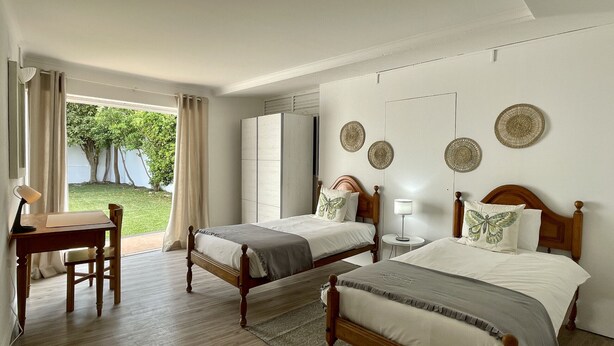 Ein Hotelzimmer mit zwei Betten, einem Schreibtisch und Blick auf einen Garten.