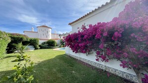 Ein weißes Gebäude mit einem Turm, umgeben von üppigem Grün und leuchtend rosa Bougainvillea.