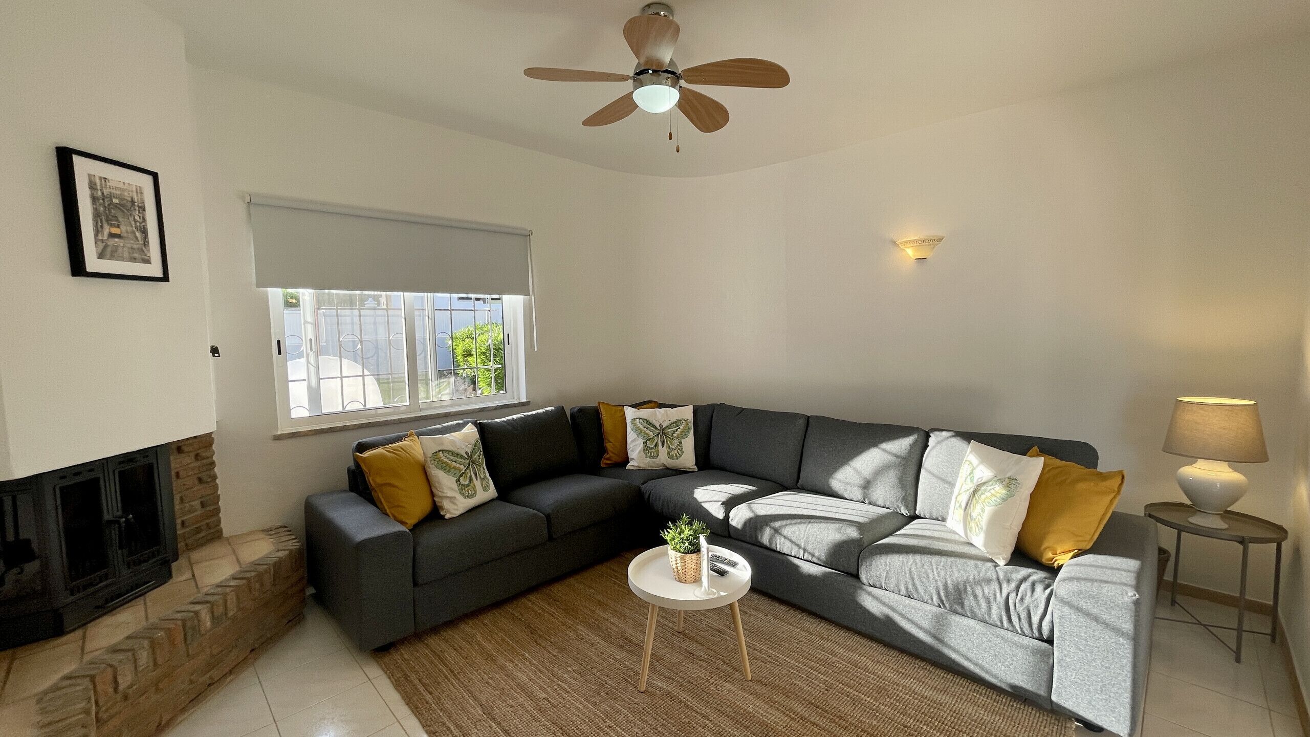 A living room with a sectional sofa, a small round table, a fireplace, and a ceiling fan.