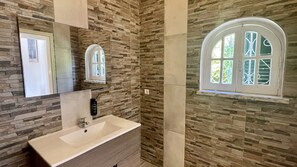 A bathroom with a stone wall, a sink, a mirror, and a window with a decorative grille. - Laranjal by Check-in Portugal (Quarteira)