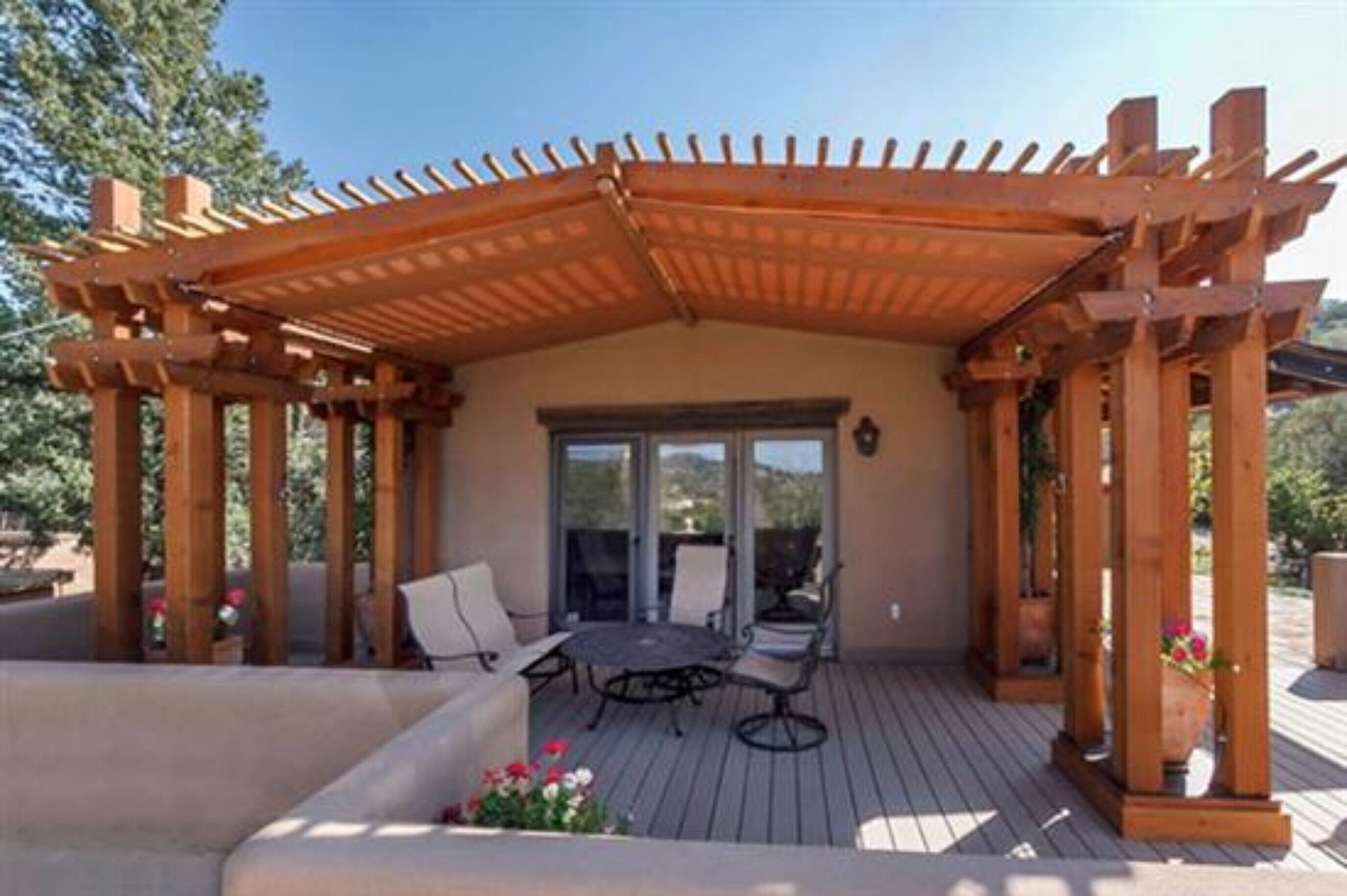 Een overdekt terras met een tafel en stoelen, een houten pergola en uitzicht op het omliggende landschap.