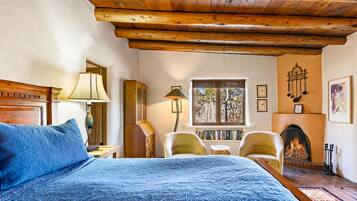 Een gezellige kamer met een houten plafond, een bed met blauw beddengoed, een open haard en een raam met uitzicht op bomen.