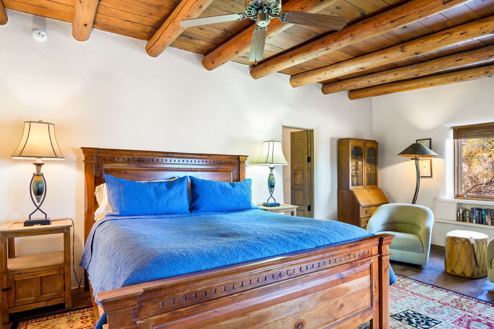 A bedroom with a wooden bed, two bedside lamps, a wooden cabinet, a chair, and a window with a view.