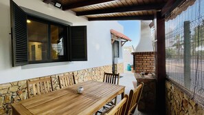 Um pátio exterior com mesa e cadeiras de madeira, um muro de pedra e um forno de tijolos.
