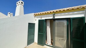 A building with white walls, green shutters, and a tiled roof.