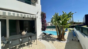 A poolside area with a table and chairs, a small tree, and a view of a swimming pool.