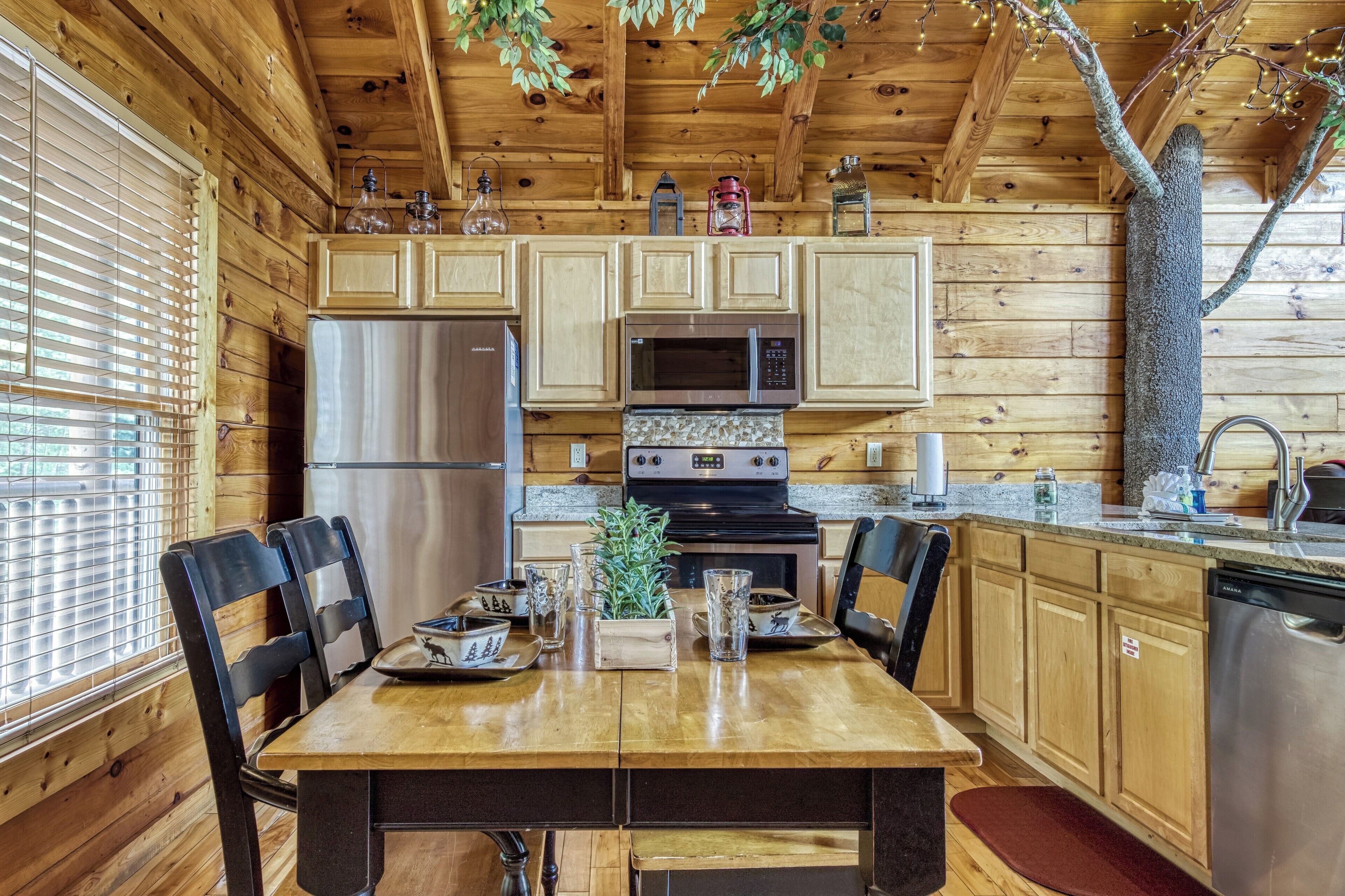 A wooden cabin kitchen with a dining table, chairs, a refrigerator, a microwave, an oven, and a sink.