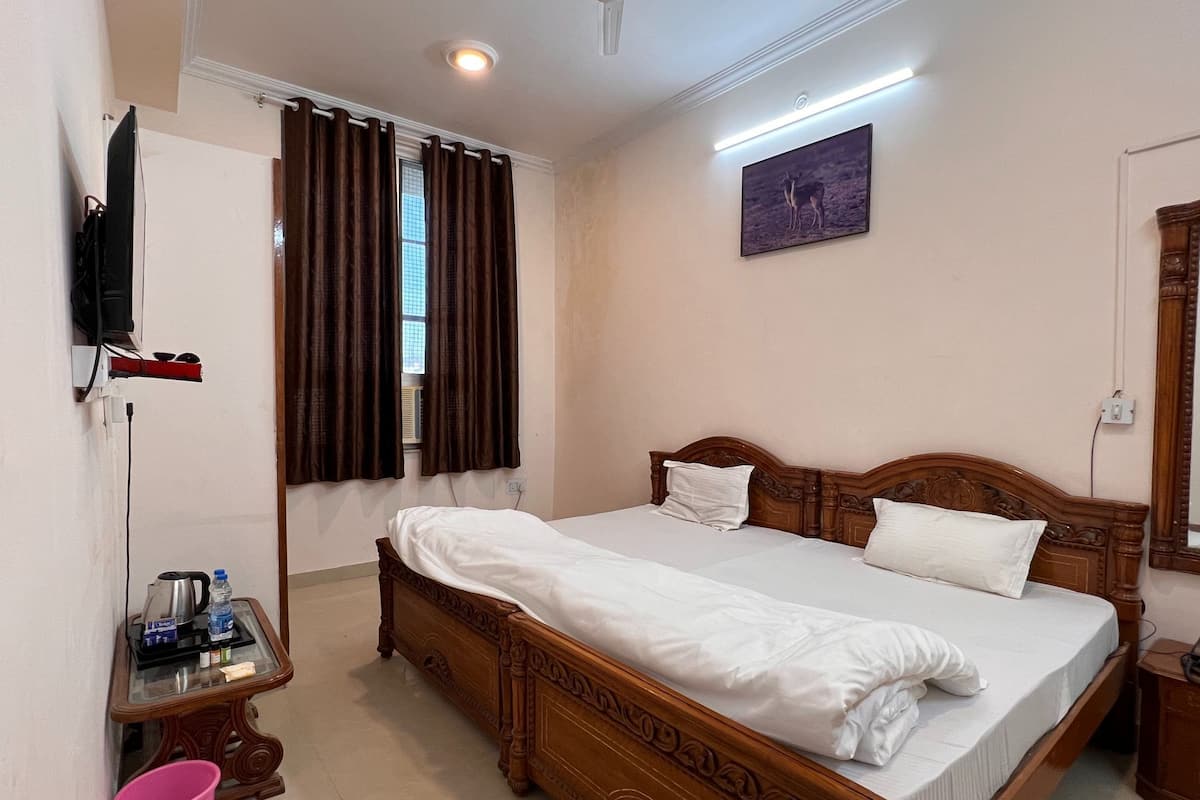 Un dormitorio con una cama grande, televisión montada en la pared, una ventana con cortinas y un cuadro sobre la cama.