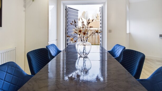 A dining area with a marble table, blue quilted chairs, and a vase with flowers. - Cosy and Luxurious House for 10 Guests in Darwen (Darwen)