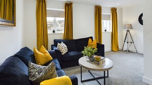 A modern living room with a dark blue sofa, yellow cushions, and a small round table with a plant. - Cosy and Luxurious House for 10 Guests in Darwen (Darwen)