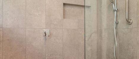 Eine moderne Dusche mit Glastür, Handbrause und am Wand montiertem Wasserhahn.