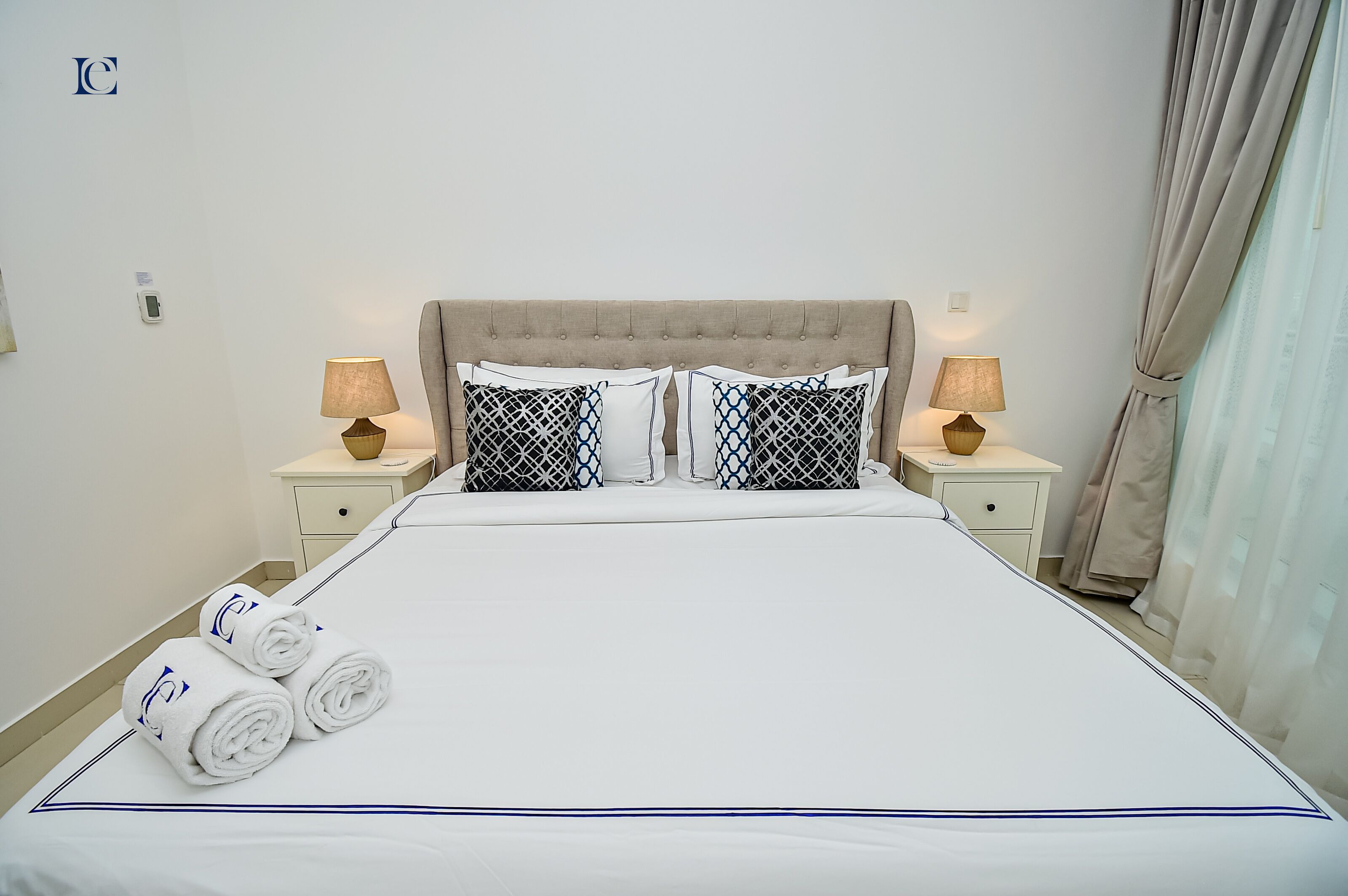 A neatly made bed with white linens and blue accents, two bedside lamps, and a headboard.
