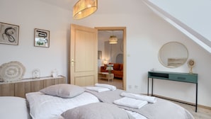 A bedroom with a loft-style ceiling, a bed with white linens, a bedside table with a lamp, and a green console table with a mirror.
