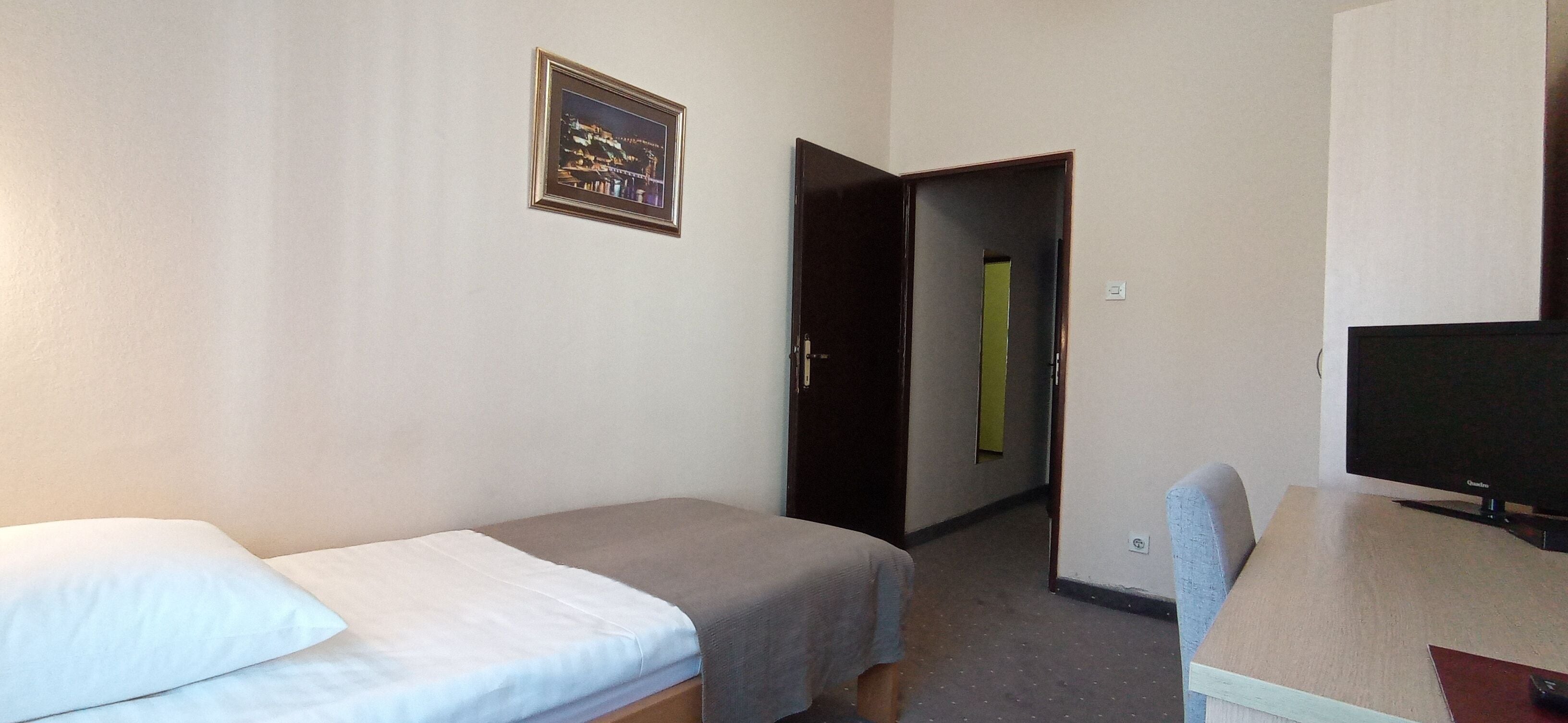 Quarto de hotel com duas camas de solteiro, televisão e um quadro na parede.