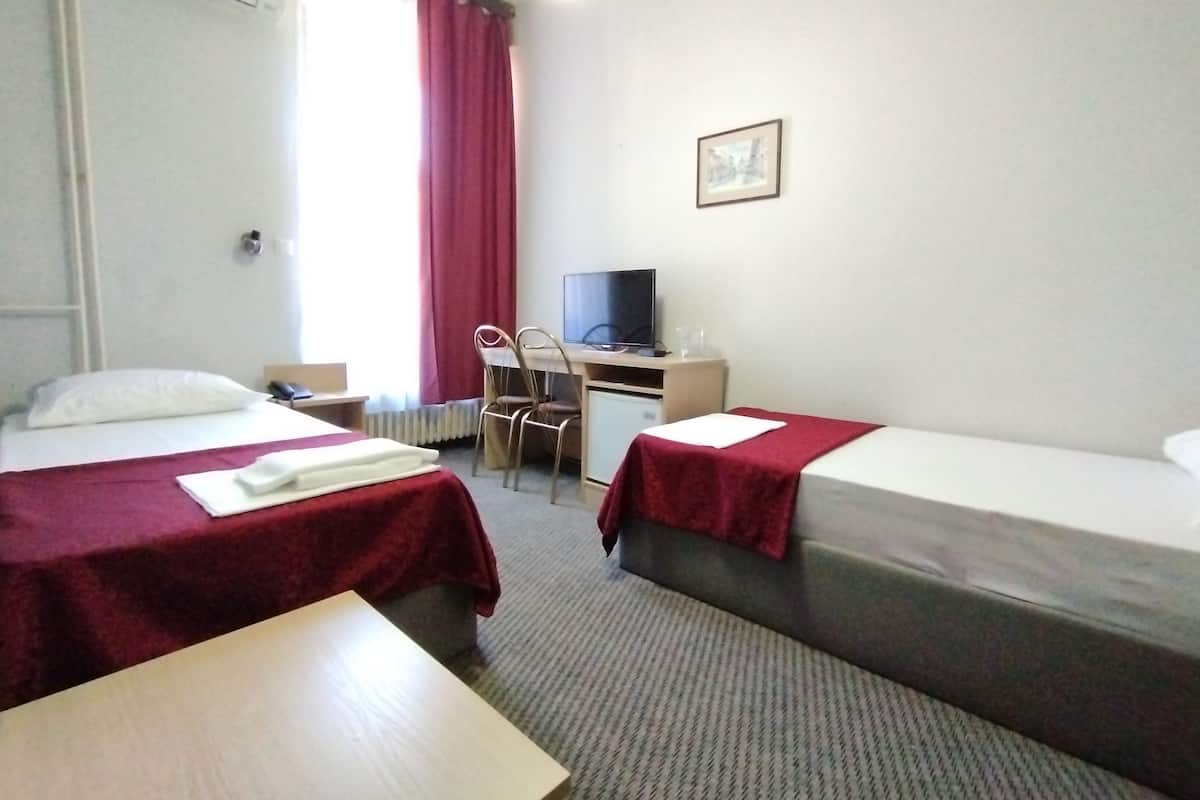 A hotel room with two beds, a desk, a chair, a television, and a radiator.