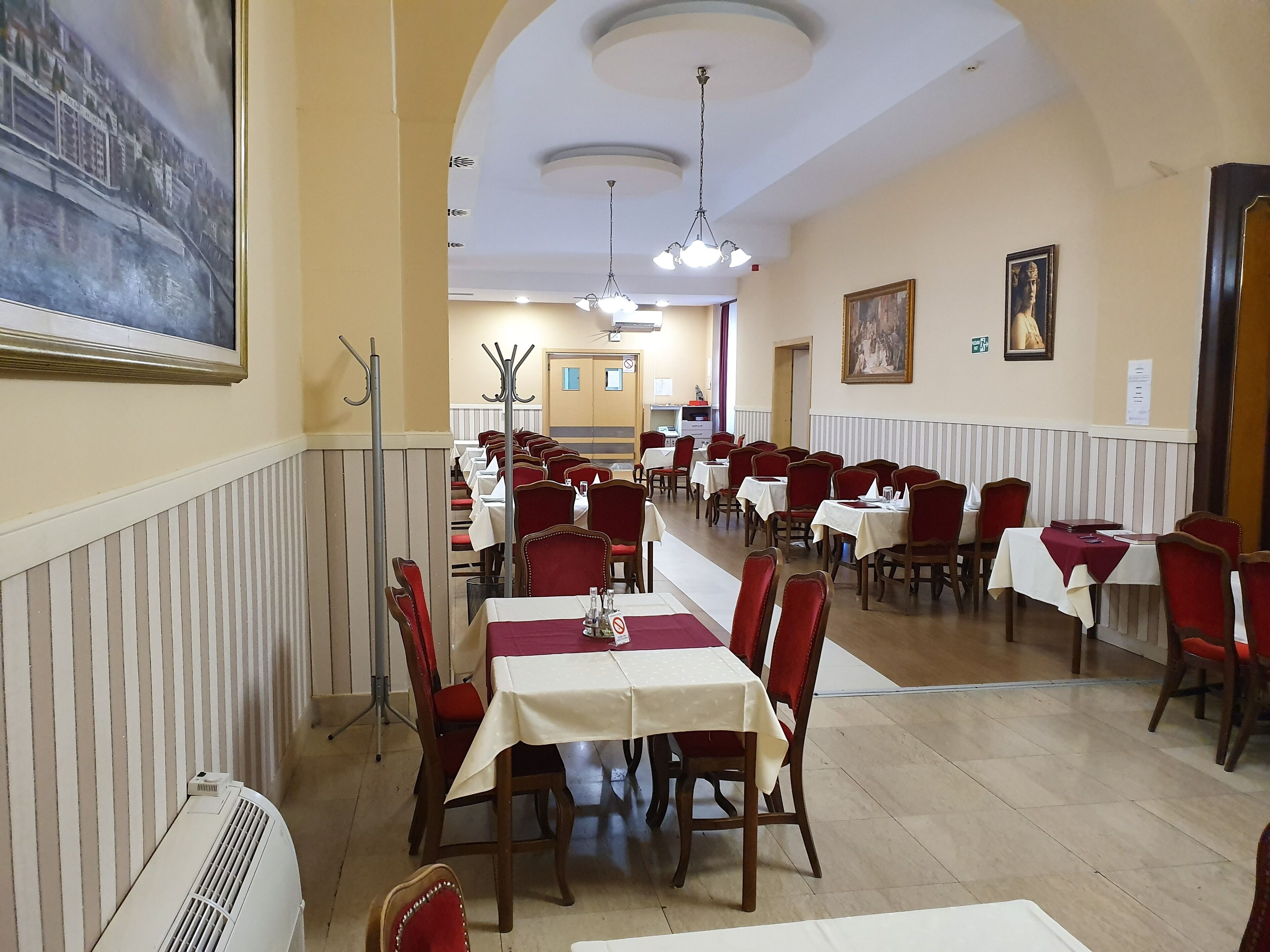 A restaurant with multiple tables and chairs, a ceiling fan, and a painting on the wall.