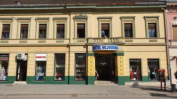 A building with a sign reading "HOTEL VOJVODINA" and multiple storefronts on the ground floor.