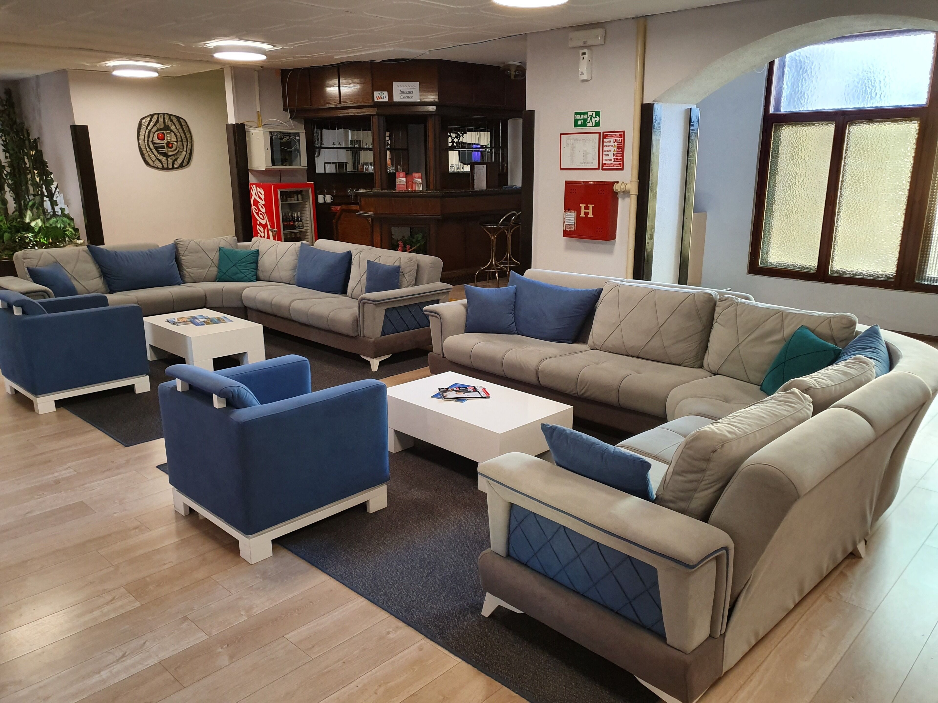 A modern lounge area with sofas, armchairs, and a coffee table. There is a vending machine, a fire extinguisher, and a window with a view.
