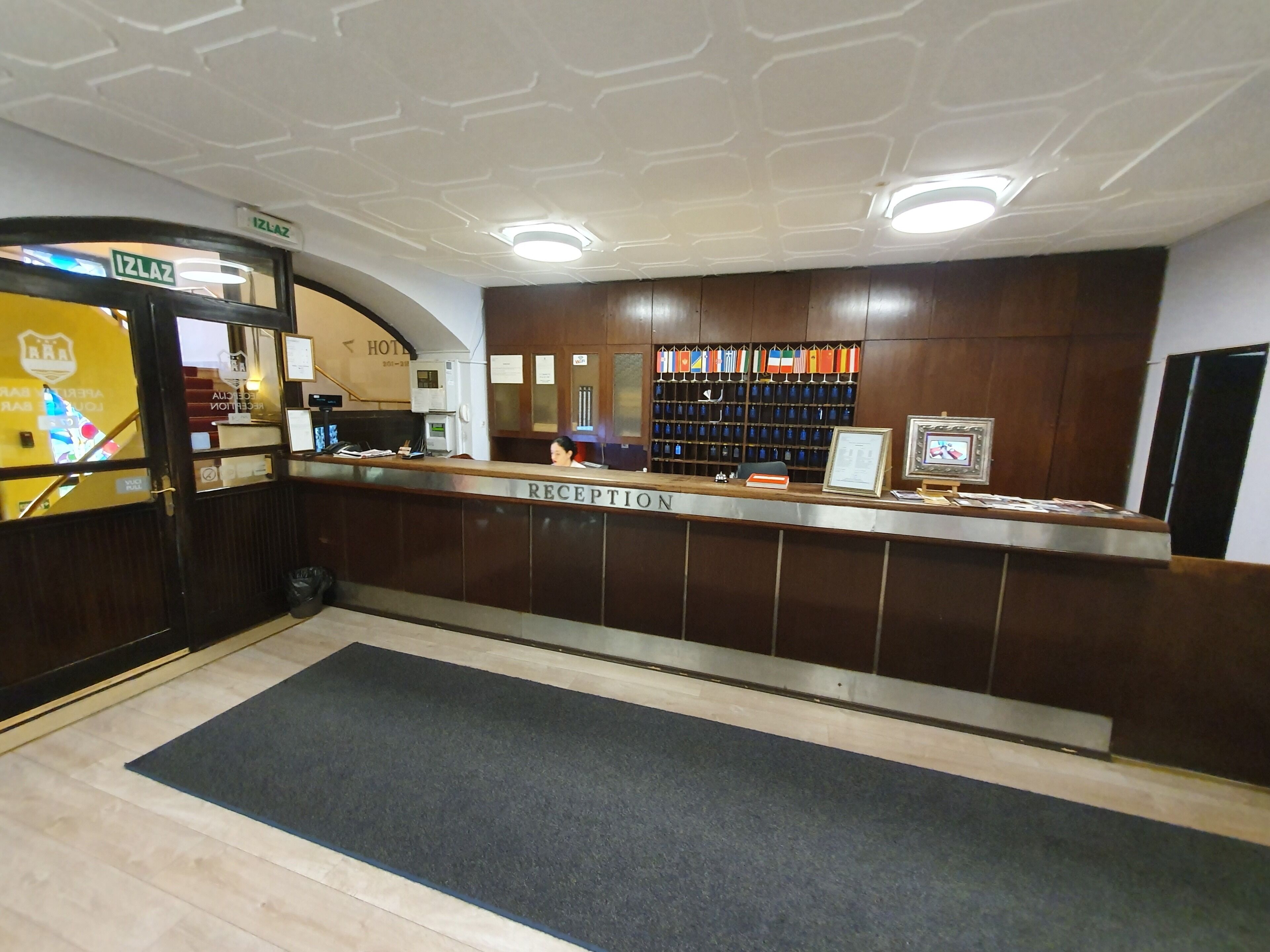 A hotel reception area with a reception desk, a wall-mounted coat rack with various items, and a sign indicating the hotel's name.