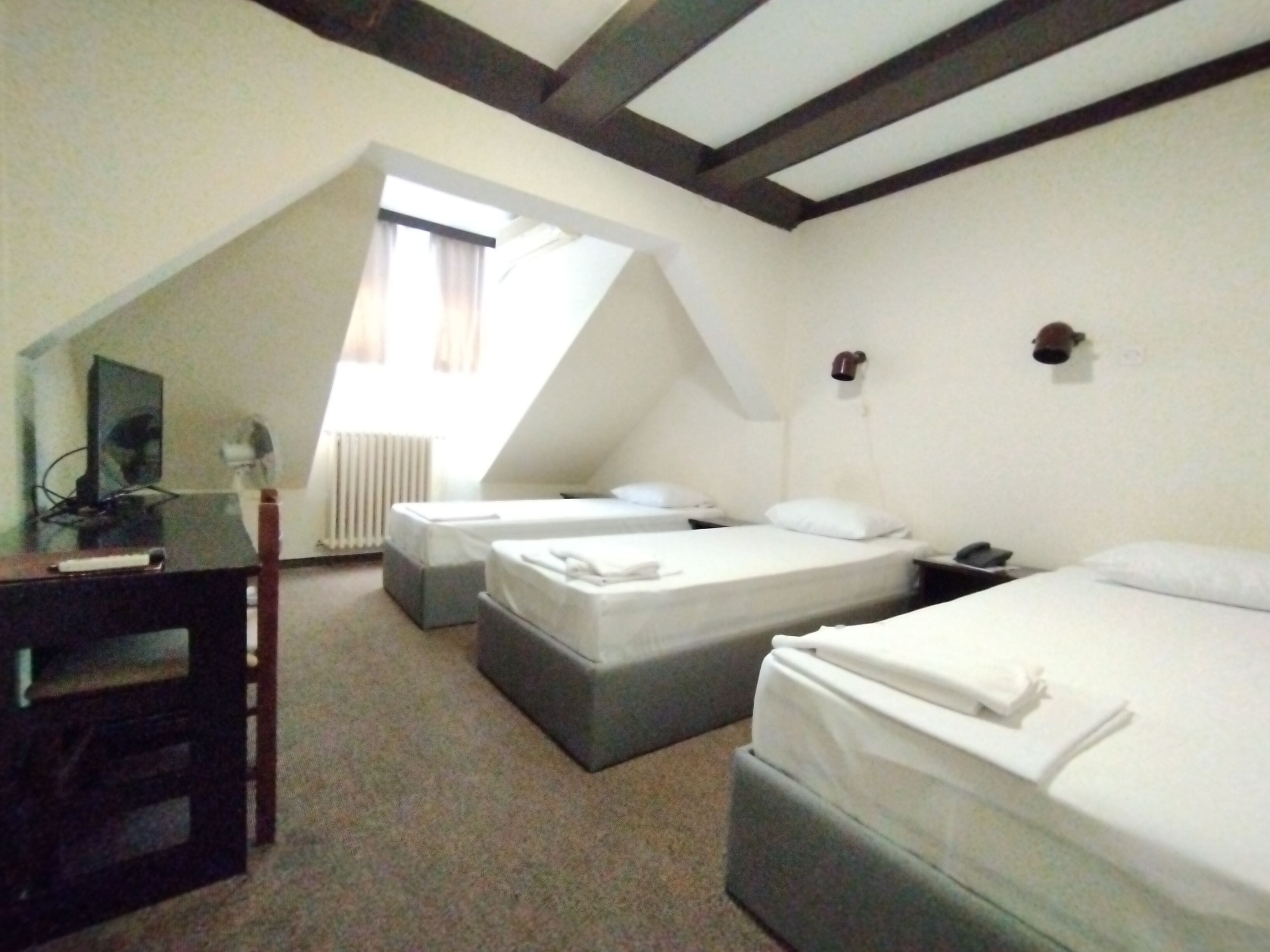 Una habitación de hotel con dos camas, un escritorio con computadora, una silla y un ventanal con cortinas.