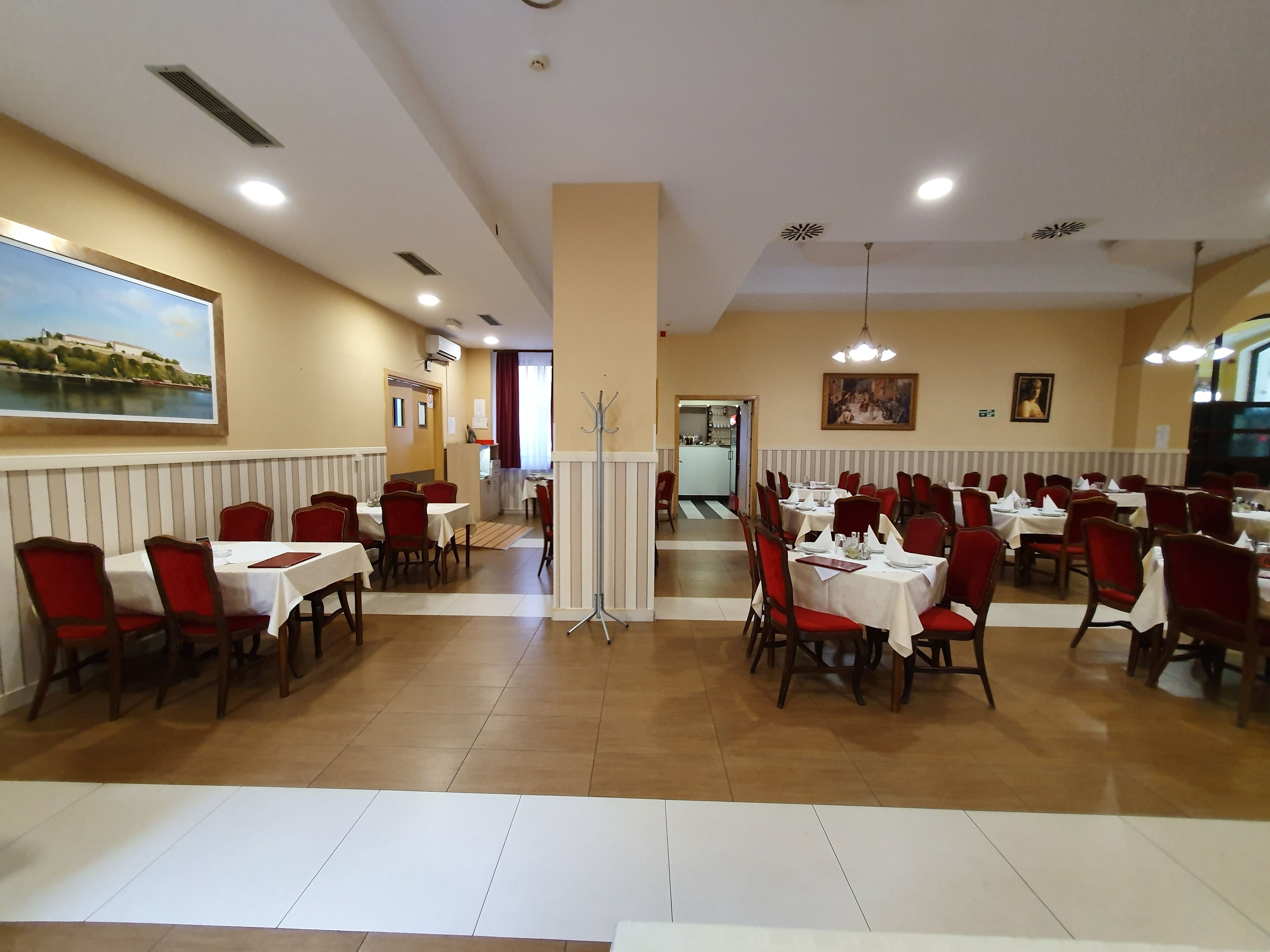 Un grand espace dédié à la salle à manger, avec plusieurs tables et chaises, un pilier central et une vue sur la cuisine en arrière-plan.