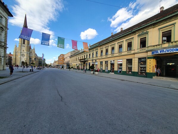 Uma rua com um hotel chamado 'HOTEL VOJVODIN' e uma igreja ao fundo.