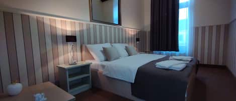A hotel room with a large bed, bedside tables, a nightstand, a mirror, and a window with curtains.