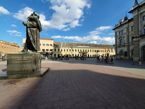 Uma praça pública com uma estátua, edifícios e céu claro.