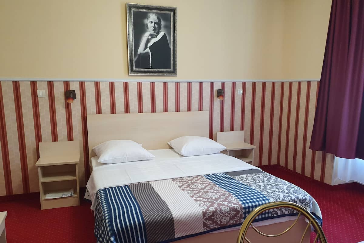 A hotel room with a bed, two bedside tables, a nightstand, a wall-mounted picture, and a red-striped wall.