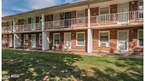 A two-story brick building with a covered front porch and a balcony on the second floor.