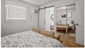 A bedroom with a bed, a window with blinds, a sliding door, and a mirror.