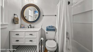 A bathroom with a white vanity, a round mirror, a toilet, and a shower curtain.