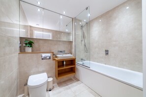 A modern bathroom with a glass-enclosed shower, a white bathtub, and a wooden vanity. - 3 Bed Flat by Limehouse Basin (London)