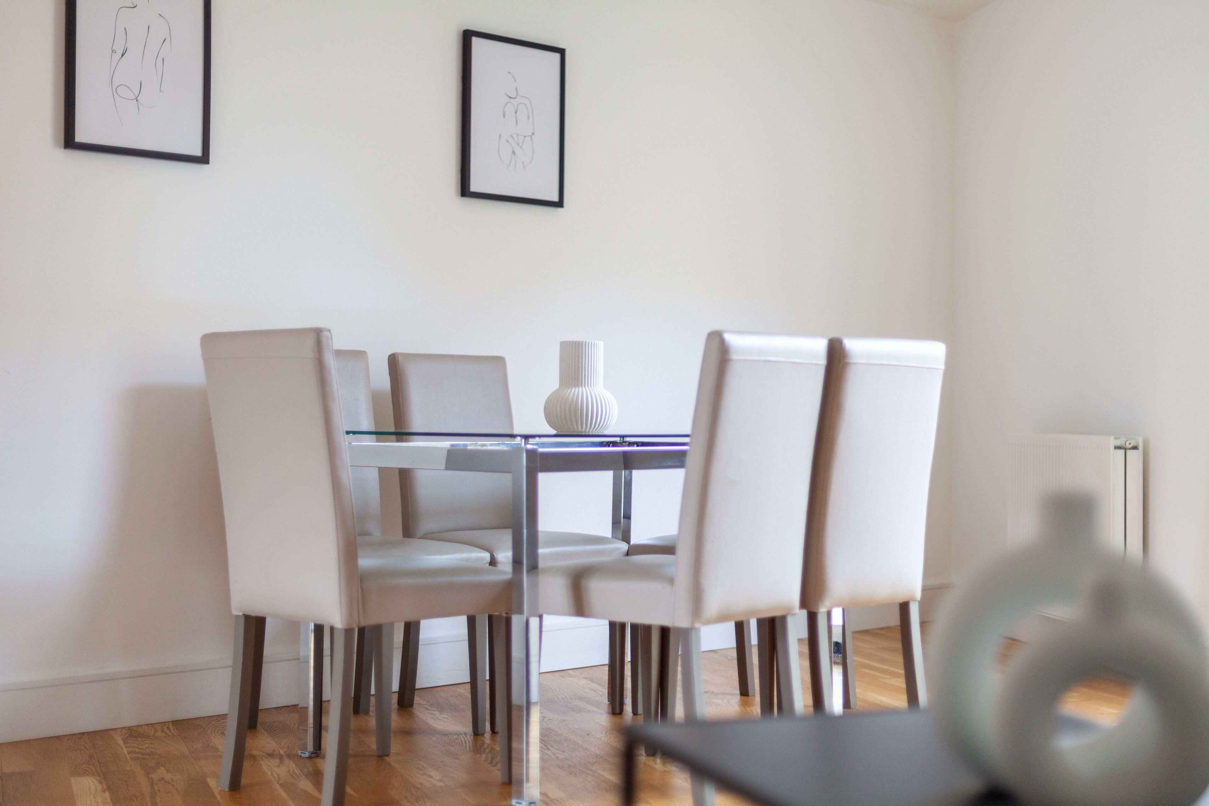 Un comedor con una mesa redonda, seis sillas y dos cuadros enmarcados en la pared.