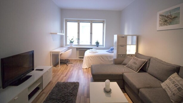 Ein modernes, helles Zimmer mit einem Bett, einem Fernseher, einem Schreibtisch und einer Couch.