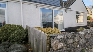 Ett hus med en grå fasad, vita detaljer och en stenmur framför.