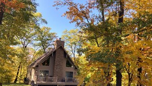 Un chalet doté d’une cheminée en pierre, d’un porche et offrant une vue sur les arbres aux couleurs automnales.