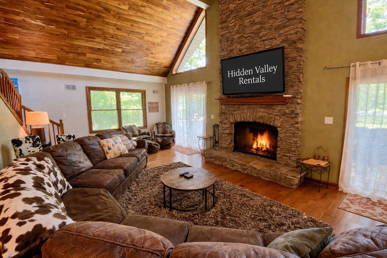 A cozy living room with a stone fireplace, leather sofas, and a flat-screen TV displaying 'Hidden Valley Rentals'.