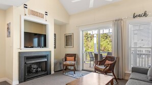 Un salon avec une cheminée, un téléviseur, des fauteuils en osier, un canapé et un balcon avec vue.