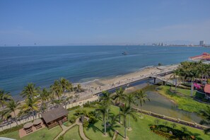 A coastal area with a beach, palm trees, a bridge, and a small water body.