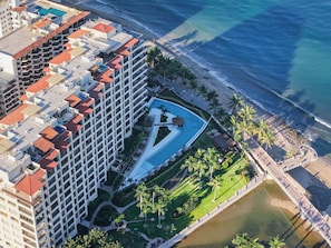 An aerial view of a hotel with a swimming pool, palm trees, and a beach.