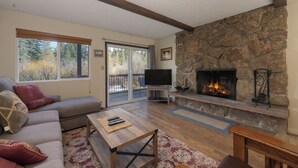 Una sala de estar con chimenea de piedra, un sofá, un televisor y un ventanal grande.