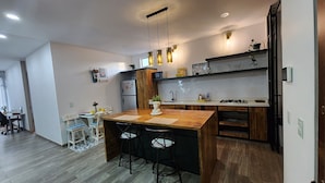 A modern kitchen with a wooden island, bar stools, a microwave, and a sink. - Edificio Pia (Bogotá)