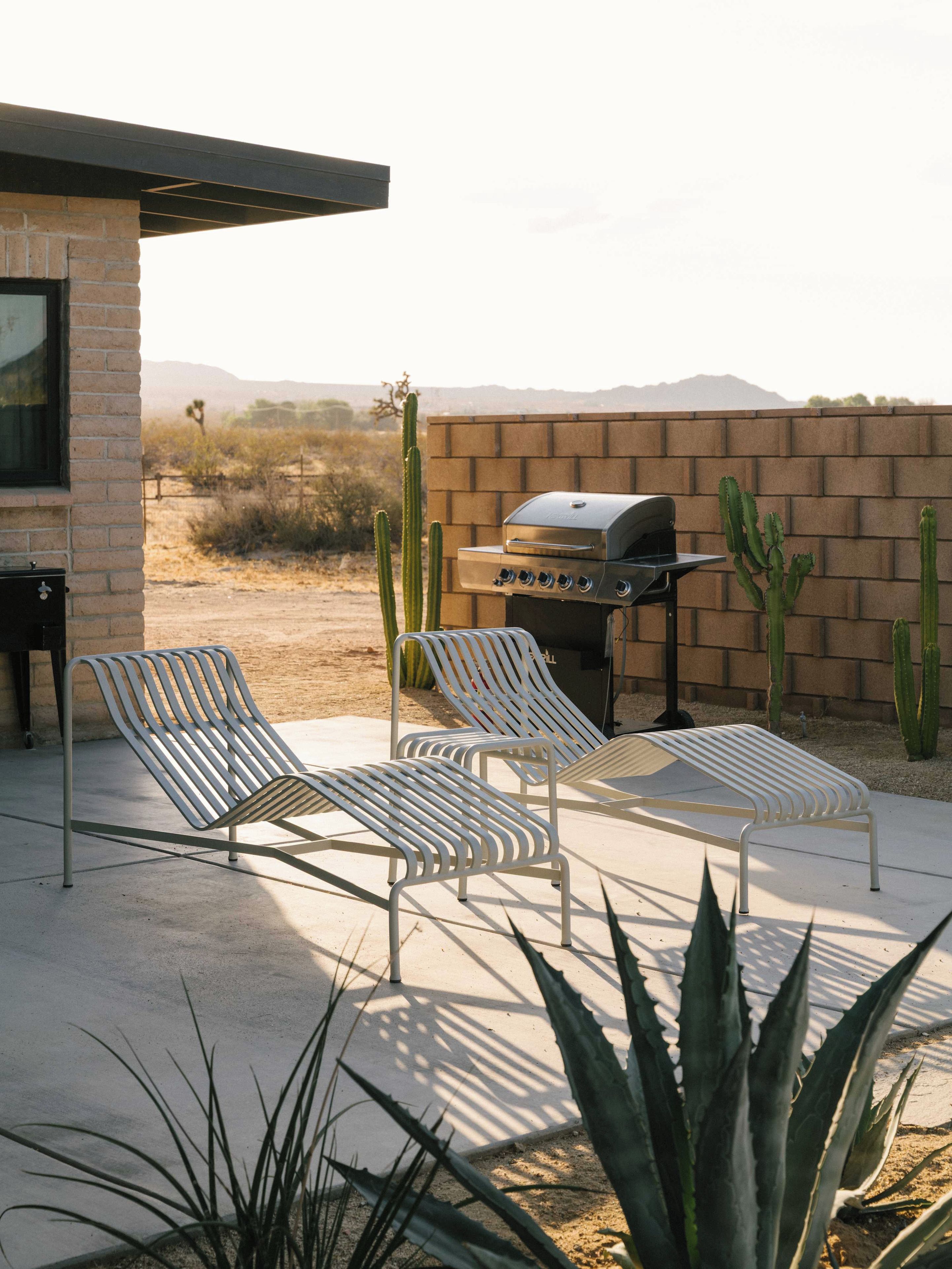 A patio with two lounge chairs, a barbecue grill, and cacti.