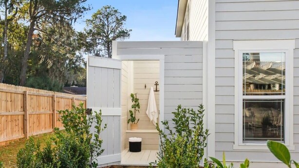 Une maison blanche avec un petit porche fermé et une clôture en bois.