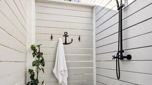 Une petite salle de bain en bois peinte en blanc, avec un banc, une plante en pot, une serviette et une pomme de douche.