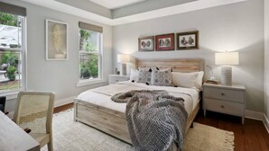Une chambre avec un grand lit, des lampes de chevet, un ventilateur de plafond et des œuvres d’art encadrées accrochées au mur.