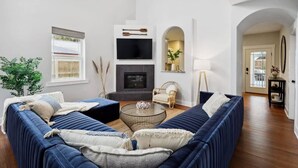 Un salon moderne avec un canapé bleu, une cheminée, un téléviseur et une grande fenêtre.