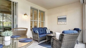A covered outdoor seating area with wicker furniture, a glass table, and a view of the sea. - Desired Pelican Landing First Floor Coach Home (Bonita Springs)
